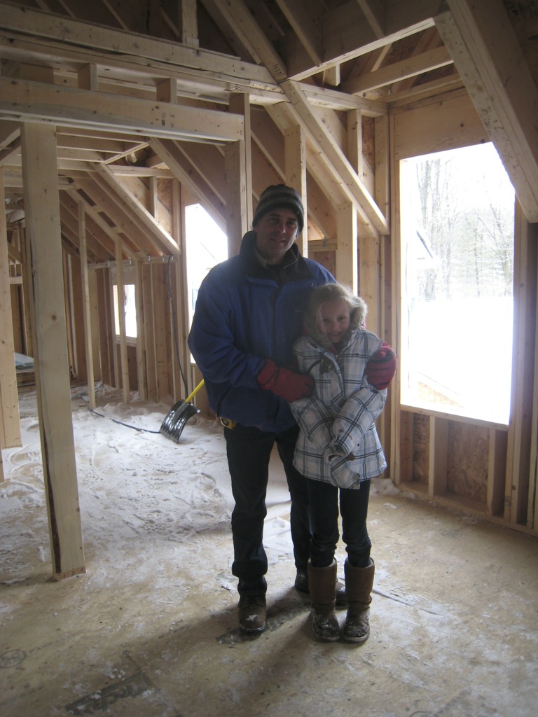 Nestor and his young daughter standing inside a newly framed house in winter